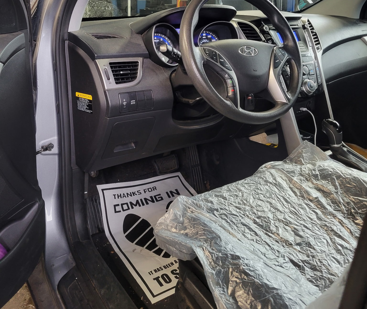 Car interior with airbag warning mat on the floor and plastic-covered seat cushion