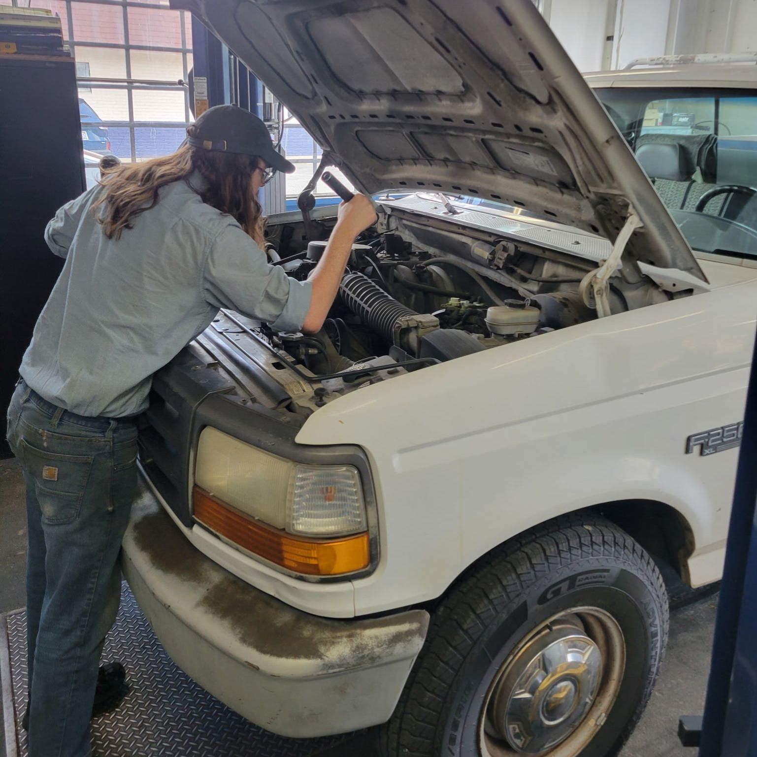 Person working under the hood of a white pickup truck in a garage.