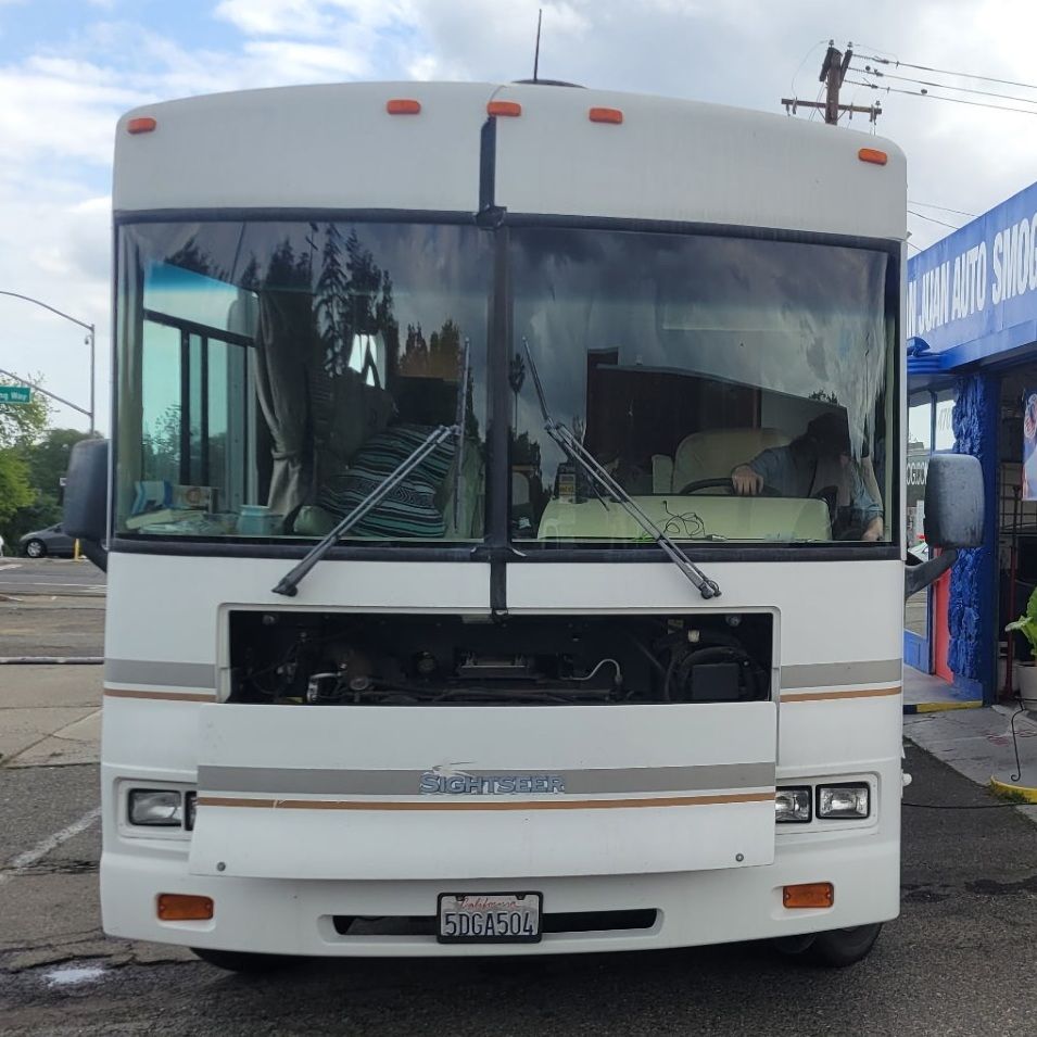 White bus with a broken front grille, parked outdoors near a blue building.